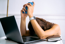 distressed woman with her head down at desk with laptop, holding her phone