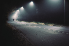 foggy road at night with one man in the far distance walking on the road