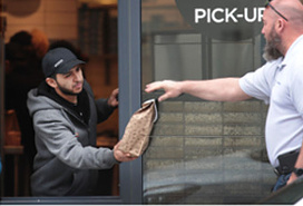 food pickup worker handing paper bag out window to customer