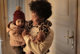 happy mom holding her tot dressed up for cold weather inside front door