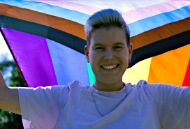 non-binary person holding a multicoloured flag overhead