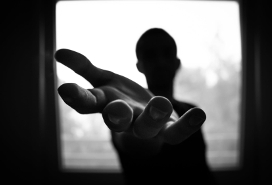 person in silhouette in front of window outstretching their hand towards viewer