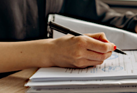 upper body of person wearing black shirt filling in a form at the top of a stack of files