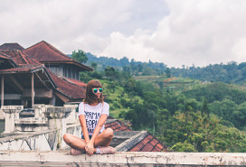 young woman sitting on a wall at an ancient location overlooking forest